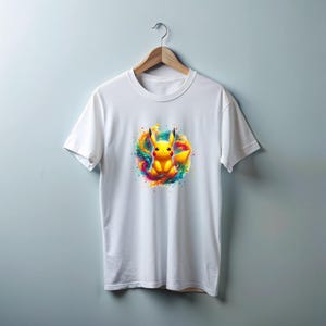 May include: White t-shirt with a colorful graphic of Pikachu, a popular cartoon character, surrounded by a splash of paint.