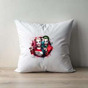 May include: White square cushion with a colourful illustration of Harley Quinn and the Joker. Harley Quinn is holding a baseball bat and wearing a red shirt with the text "Harley & Suicide". The Joker is wearing a red suit and green hair.