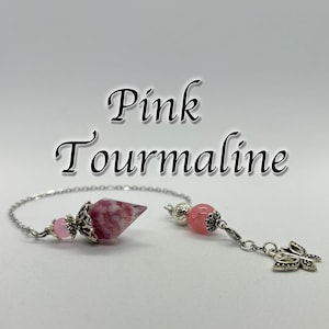 Może przedstawiać: Wahadło z różowego turmalinu z srebrnym łańcuszkiem i różową koralikiem z kryształu. Wahadło to spiczasty kryształ z srebrną czapką. Koralik to okrągły kryształ z srebrną czapką. Łańcuszek jest przymocowany do koralika i wahadła.