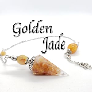 May include: Golden Jade crystal pendulum with a silver chain and a silver charm. The pendulum is a cone shape with a pointed tip and is made of clear quartz with golden jade crystals embedded in it.