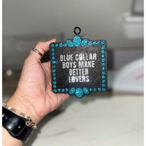 May include: Black square sign with a blue glitter border and the text "BLUE COLLAR BOYS MAKE BETTER LOVERS" in white lettering.