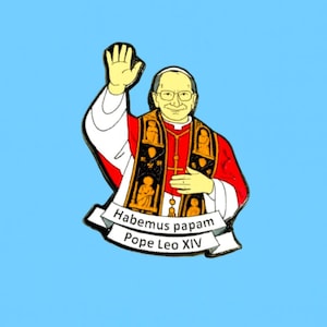 May include: A colourful enamel pin depicting Pope Leo XIV waving. The pin features a red and white robe, black vestments, and the text "Habemus papam" and "Pope Leo XIV" on a banner.