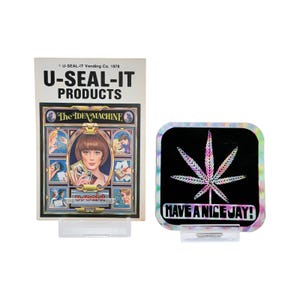 May include: Two vintage vending machine products. One is a booklet titled "U-SEAL-IT PRODUCTS" with "The IDEA MACHINE" on the front. The other is a square sticker with a rainbow cannabis leaf on a black background and the text "HAVE A NICE JAY!"