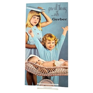 May include: Vintage Gerber advertisement featuring three children. A baby rests in a wicker bassinet on a scale, while two older children pose with a book and raised arms. The text reads "grow all the way...with Gerber."
