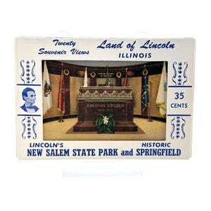 May include: A vintage souvenir card featuring a depiction of Abraham Lincoln's tomb in New Salem State Park, Illinois. The card includes the text "Land of Lincoln" and "Twenty Souvenir Views". The card also displays the price of "35 CENTS".