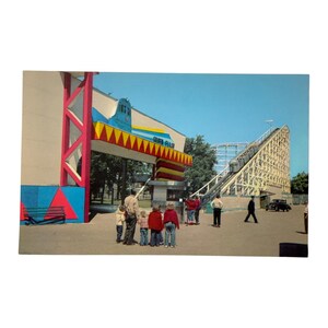 May include: Vintage postcard featuring a roller coaster and entrance archway at Silver Falls. The arch is red, blue, and yellow, with the words "Silver Falls" on it. People are standing in front of the entrance and the roller coaster.