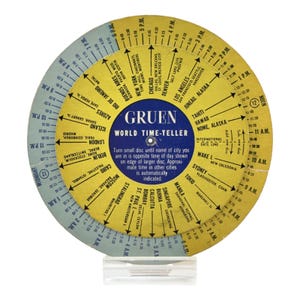 May include: A vintage Gruen World Time-Teller, a circular time zone calculator. The device, mounted on a clear stand, features two rotating discs with city names and corresponding time zones. The text "Gruen World Time-Teller" is visible.