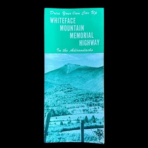 Puede incluir: Un folleto vintage en tonos turquesa y blanco. La sección superior presenta el texto "Drive Your Own Car Up WHITEFACE MOUNTAIN MEMORIAL HIGHWAY In the Adirondacks". La parte inferior muestra un paisaje montañoso.