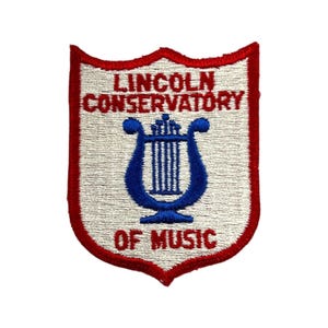May include: Embroidered patch with a red border and a white background. The patch features the text "LINCOLN CONSERVATORY OF MUSIC" in red, with a blue harp design in the center. The patch is shield-shaped.