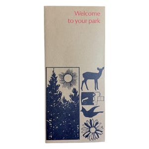 May include: A tan brochure with the text "Welcome to your park" in pink. The brochure features blue illustrations of trees, a sun, a deer, a camera, a bird, and a flower. The brochure is rectangular and vertically oriented.