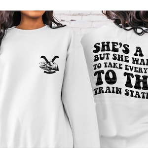 Op de afbeelding: Witte trui met een zwarte afbeelding op de voorkant en de tekst "She's a 10 but she wants to take everyone to the train station" op de achterkant.