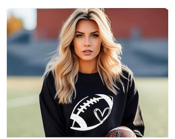May include: A black sweatshirt with a white graphic of a football with a heart inside. The model has long blonde hair.