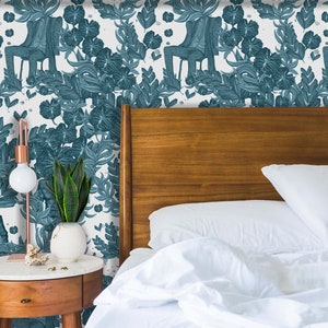 May include: Teal and white wallpaper featuring a repeating pattern of a figure in a suit and chair surrounded by stylized leaves. A wooden headboard and a nightstand with a lamp and plant are in the foreground.