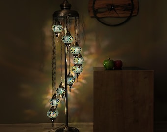 May include: A tall floor lamp with a dark bronze-colored metal stand and base, featuring nine hanging mosaic glass globes in shades of blue, green, and yellow. The globes are arranged in a spiral pattern, each suspended by a thin metal chain.