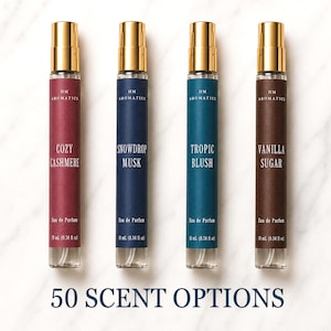 May include: Four cylindrical glass perfume spray bottles with gold caps, labeled HM Aromatics. The scents are Cozy Cashmere, Snowdrop Musk, Tropic Blush, and Vanilla Sugar. Each bottle contains 10 mL (0.34 fl oz) of Eau de Parfum. Text reads 50 SCENT OPTIONS.