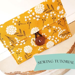 May include: A yellow fabric clutch with a white floral pattern and a brown button closure.  Sewing Tutorial.