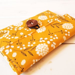 May include: A yellow fabric pouch with a white floral pattern and a brown button closure.