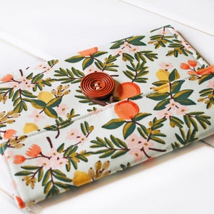 May include: A light blue fabric clutch with a floral print featuring lemons, oranges, and pink flowers. The clutch has a brown button closure.