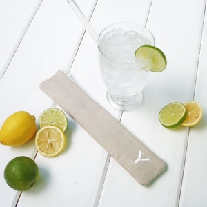 May include: A beige fabric case with a white "Y" on it, a glass of water with ice and lime slices, and lemons and limes on a white wooden surface.