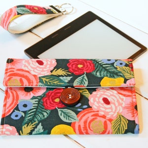 May include: A floral patterned fabric case with a brown button closure. The case is designed to hold an e-reader.