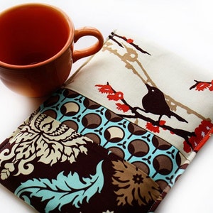 May include: A brown, beige, and turquoise fabric pouch with a black bird design and red flowers. The pouch is made of patchwork fabric and has a quilted texture.
