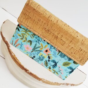 May include: A light blue floral patterned clutch with a cork exterior. The clutch has a gold accent on the cork.