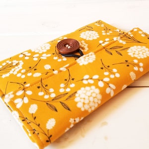 May include: A yellow fabric pouch with a white floral pattern and a brown button closure.