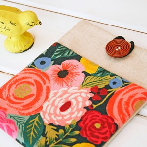 May include: A floral fabric pouch with a beige flap and a brown button closure. The pouch features a dark green background with a colorful floral pattern.