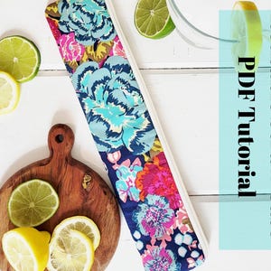 May include: A colorful floral fabric case for reusable straws. The case has a white zipper and is lying on a white wooden surface. The text "Reusable Straw Case PDF Tutorial" is written on a light blue background.