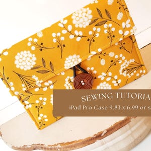 May include: A yellow fabric iPad case with a white floral pattern and a brown button closure. The case is sitting on a white wooden surface. Sewing Tutorial iPad Pro Case 9.83 x 6.99 or smaller.