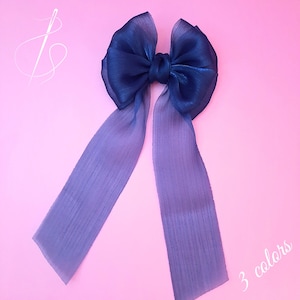 May include: A large blue ombre ribbon bow with long tails. The bow is made of sheer fabric and has a slight shimmer.  "3 colours" is written in white text on the bottom right corner of the image.