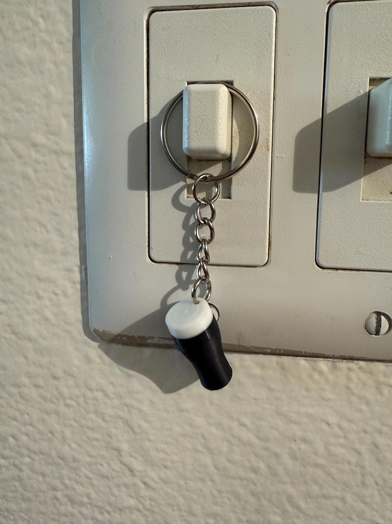 Pu&ograve; includere: Un portachiavi a forma di bicchiere da pinta in miniatura, bianco e nero. Il portachiavi &egrave; attaccato a una catena d'argento. Il bicchiere da pinta ha un corpo nero e una parte superiore bianca, che ricorda una birra stout.