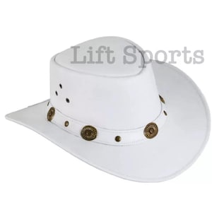May include: A white leather cowboy hat with a brown leather band and decorative metal accents. The hat has a wide brim and a tall crown.