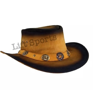 May include: A brown leather cowboy hat with a black brim and decorative metal accents. The hat has a faded, distressed look.