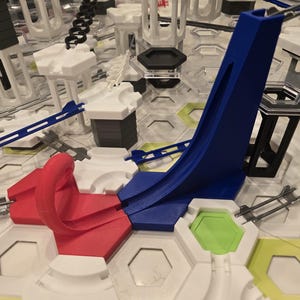 Könnte beinhalten: Ein farbenfrohes Murmelbahn-Konstruktionsset mit verschiedenen Komponenten. Das Set enthält weiße, schwarze, rote, blaue und grüne Teile. Das Design umfasst Bahnen, Türme und sechseckige Grundplatten, wodurch eine komplexe Struktur entsteht.