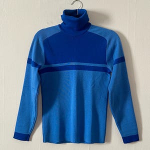May include: A blue and light blue striped turtleneck sweater. The sweater has a ribbed texture and a long sleeve.