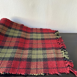 May include: Red, green, and black plaid woven table runner with fringed edges.