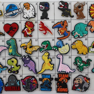 May include: A set of 35 colorful dinosaur-themed shoe charms. The charms feature various dinosaurs, including a Tyrannosaurus Rex, Triceratops, Stegosaurus, and Velociraptor. Some charms have the words "Jurassic Park" on them.