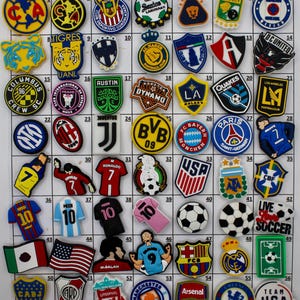 May include: A collection of colorful soccer-themed charms featuring team logos, flags, and player jerseys. Includes logos for teams like Juventus, FC Barcelona, and Manchester City. Perfect for decorating shoes or accessories.