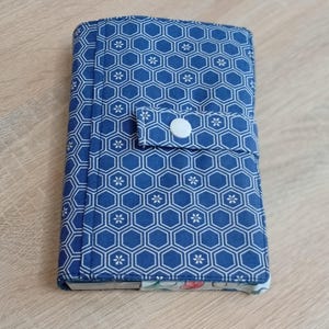 May include: A blue fabric journal cover featuring a white hexagonal pattern and small white flower accents. It has a white button closure and a floral patterned edge.
