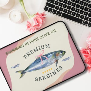 May include: A pink and cream colored laptop sleeve with a watercolor illustration of a sardine swimming in olive oil. The text "Swimming in Pure Olive Oil" and "Premium Sardines" is printed on the sleeve.