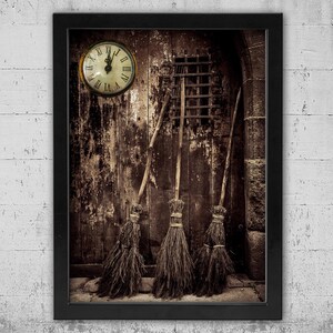 May include: A framed sepia-toned print featuring a weathered wooden door with three rustic brooms leaning against it. A round clock with Roman numerals hangs above. The image evokes a vintage, possibly Halloween, theme.