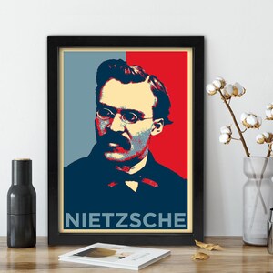 May include: Framed poster featuring a pop art style portrait of Friedrich Nietzsche. The image has a color block design with blue, red, and beige tones. The name "NIETZSCHE" is printed in white at the bottom of the poster.