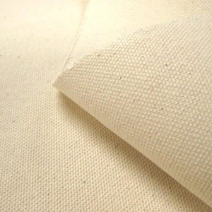 Puede incluir: Primer plano de una tela de lona natural, que muestra la textura tejida y el color blanquecino. La tela est&aacute; doblada, revelando el reverso. Ideal para proyectos art&iacute;sticos, tapicer&iacute;a o manualidades.