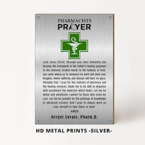 Op de afbeelding: Zilveren metalen print met de tekst "PHARMACISTS PRAYER" en een groen kruis met een slangensymbool. De print bevat een gebed en de naam Gregor Lovato, Pharm.D.