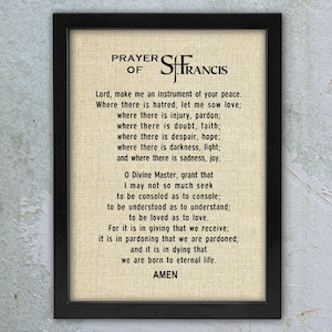 Op de afbeelding: Een ingelijste print met het "Gebed van Sint Franciscus" in zwarte tekst op een beige achtergrond. De zwarte lijst omringt de tekst, inclusief de verzen van het gebed en het afsluitende "Amen".