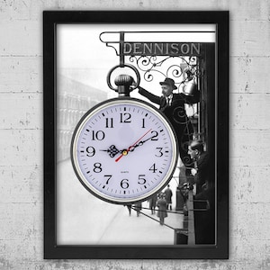Può includere: Orologio da parete con cornice nera con una fotografia vintage in bianco e nero. Il quadrante dell'orologio è bianco con numeri e lancette nere. La fotografia presenta una scena di strada con la scritta "DENNISON" in alto.