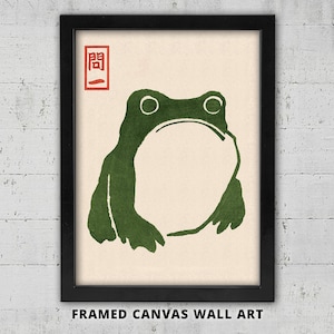 Könnte beinhalten: Gerahmtes Leinwandbild mit einer grünen Frosch-Illustration im minimalistischen Stil. Der Frosch hat einen großen, offenen Mund und einfache Linien. Das Kunstwerk enthält japanischen Text in einem roten Quadrat oben links.