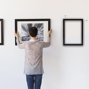 Puede incluir: Una persona sostiene una fotograf&iacute;a de paisaje en blanco y negro enmarcada. Se ven otras dos obras de arte enmarcadas. Tambi&eacute;n se muestra un marco negro vac&iacute;o, de 30 x 40 cm. Los marcos tienen un dise&ntilde;o sencillo y moderno.