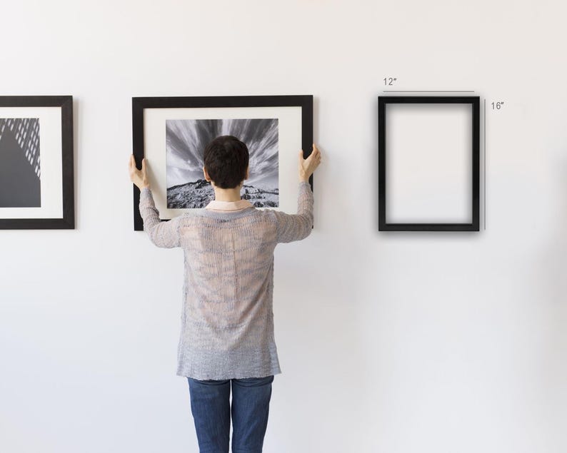Puede incluir: Una persona sostiene una fotograf&iacute;a de paisaje en blanco y negro enmarcada. Se ven otras dos obras de arte enmarcadas. Tambi&eacute;n se muestra un marco negro vac&iacute;o, de 30 x 40 cm. Los marcos tienen un dise&ntilde;o sencillo y moderno.
